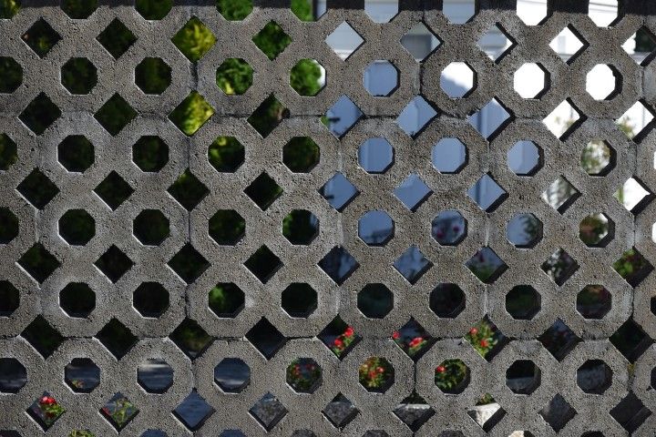 Concrete grid wall with hexagonal cutouts revealing a blurry background of greenery and bright flowers.