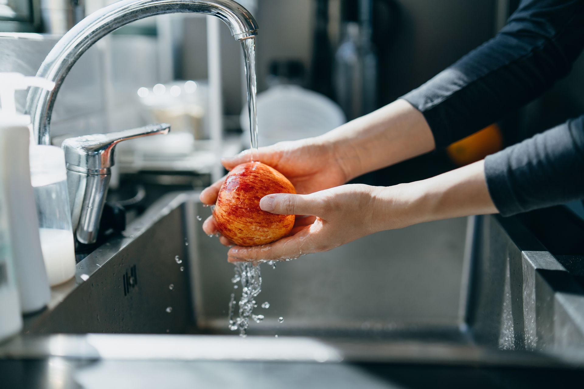 A person is washing an apple in a kitchen sink.
