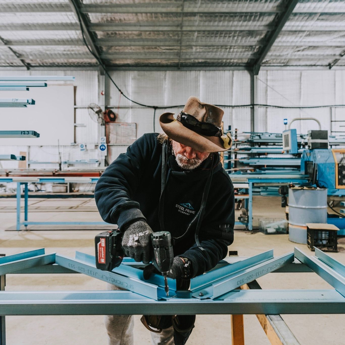 A Man Wearing a Cowboy Hat is Working on a Piece of Metal — Steel Frame Company In Parkes, NSW