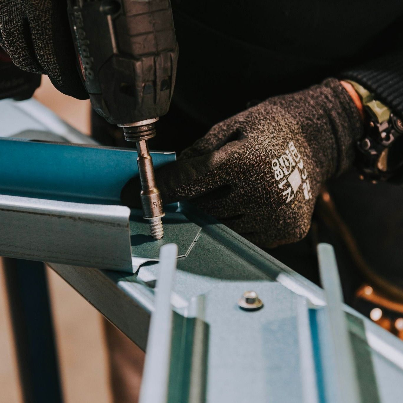 A Person Wearing Gloves is Using a Drill on a Piece of Metal — Steel Frame Company In Tamworth, NSW
