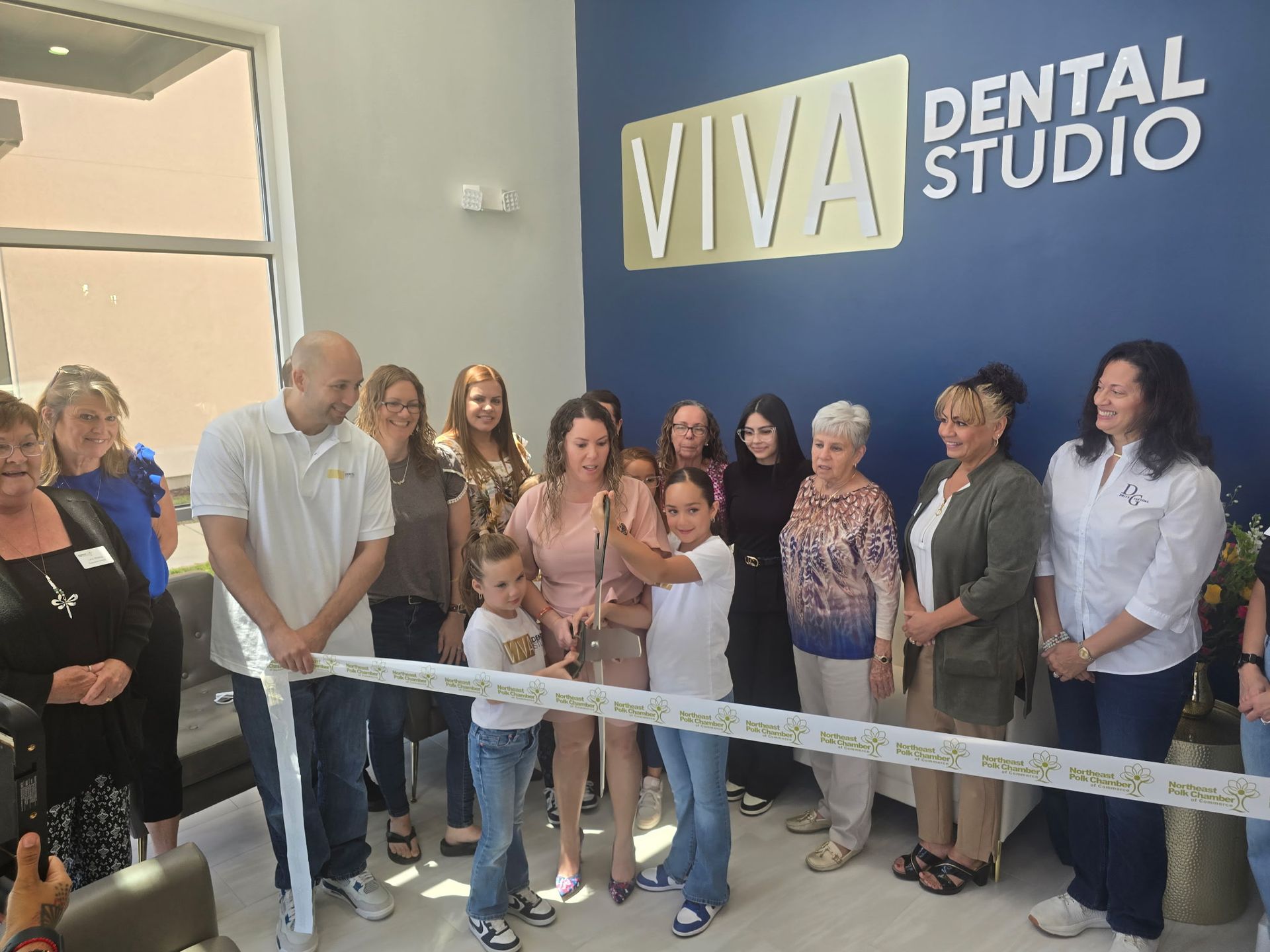 People cutting a ribbon at the grand opening of Viva Dental Studio. Blue wall, gold sign, diverse group smiling.