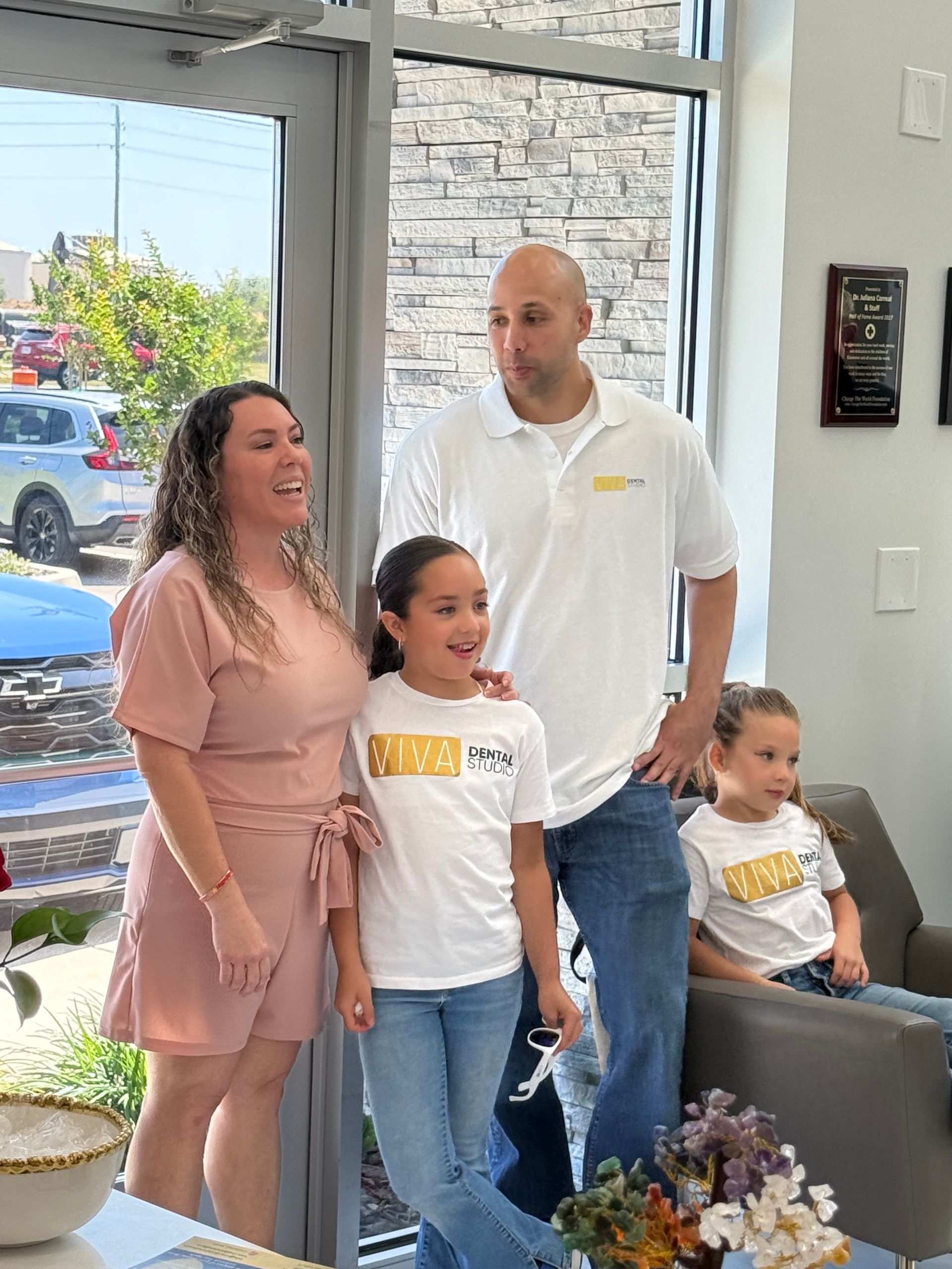 Family of four poses inside a shop. Woman in pink dress, man in white shirt, two girls in matching tees.