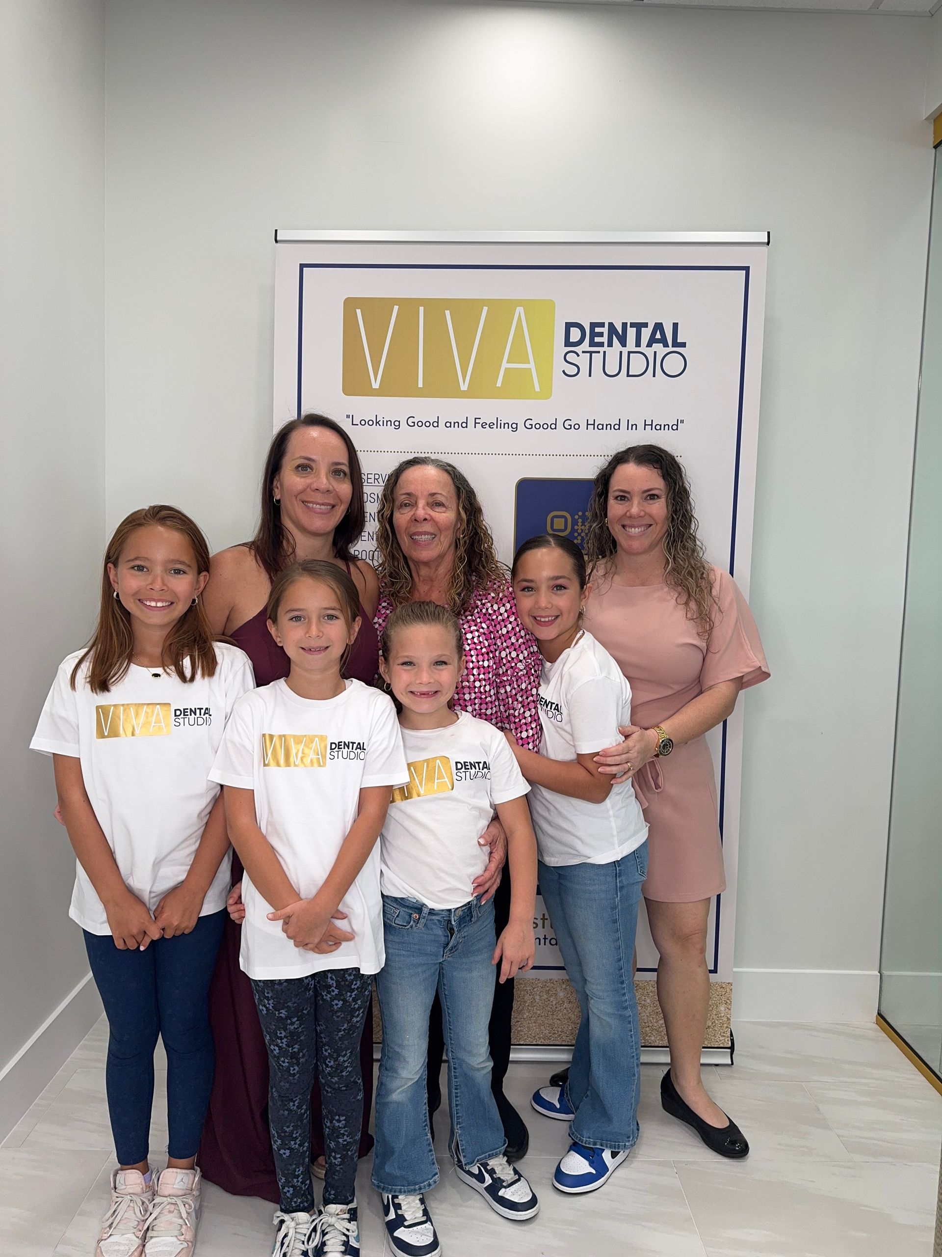 Group of seven people at Viva Dental Studio: adults and children smiling, banner in background.