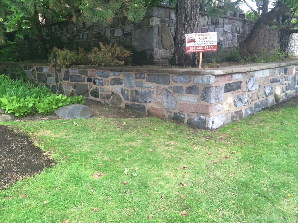 Un mur de pierre avec une pancarte devant.