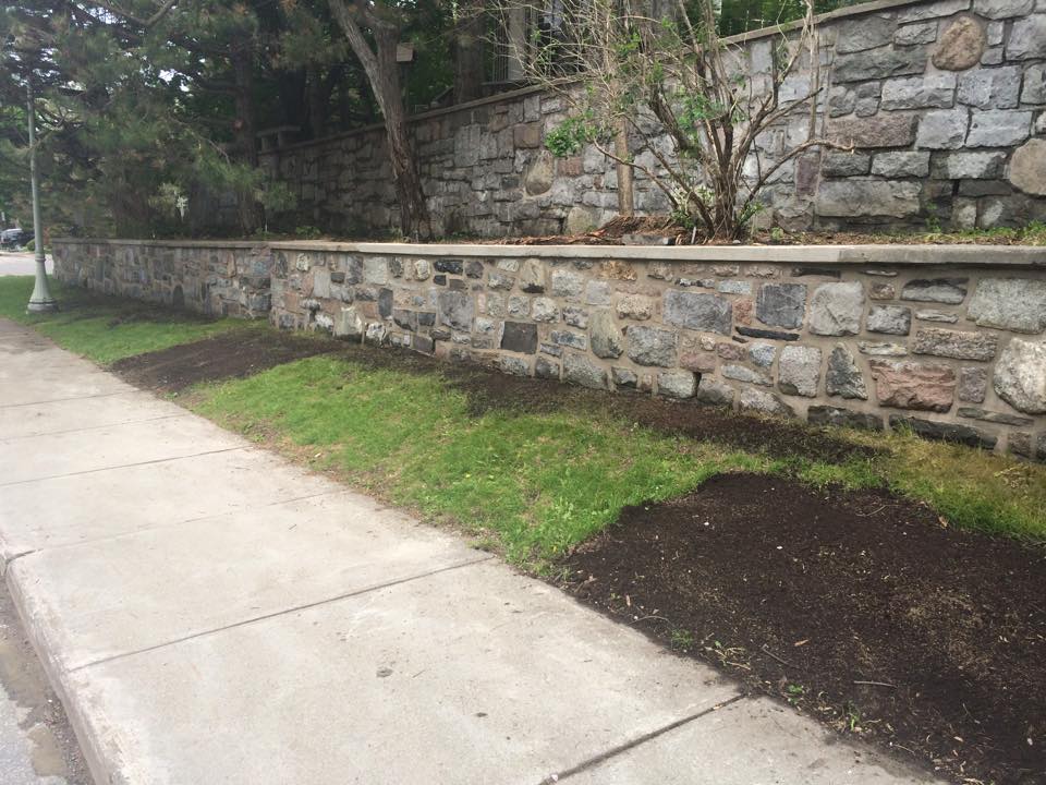 Un mur de pierre entoure une pelouse verdoyante sur le côté d'un trottoir.