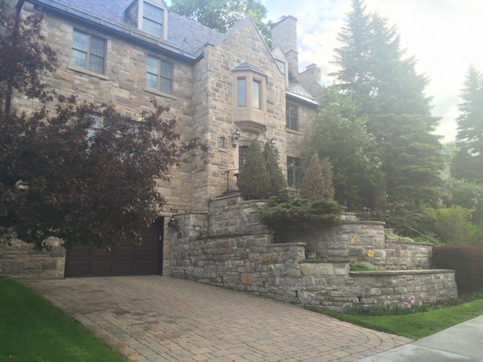 Une grande maison en pierre avec une allée en brique et des arbres devant.