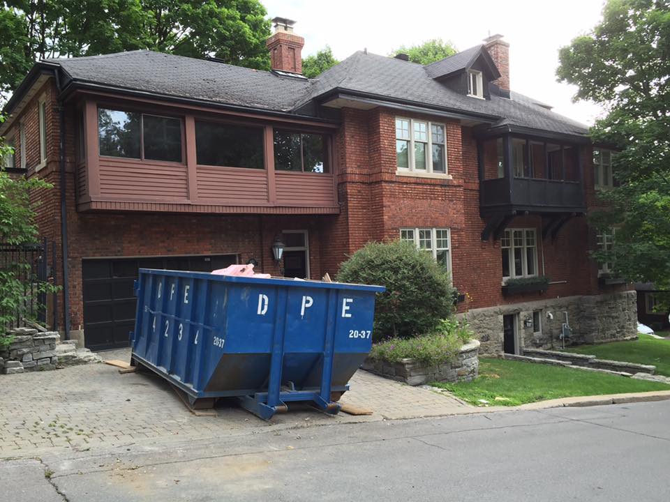 Une grande maison en brique avec une benne à ordures bleue devant
