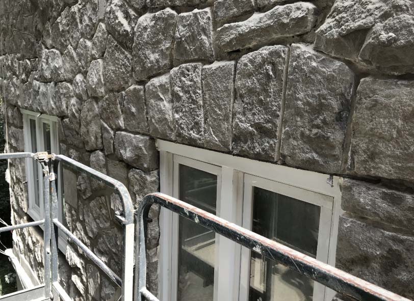 Un mur en pierre avec deux fenêtres et une rampe métallique.