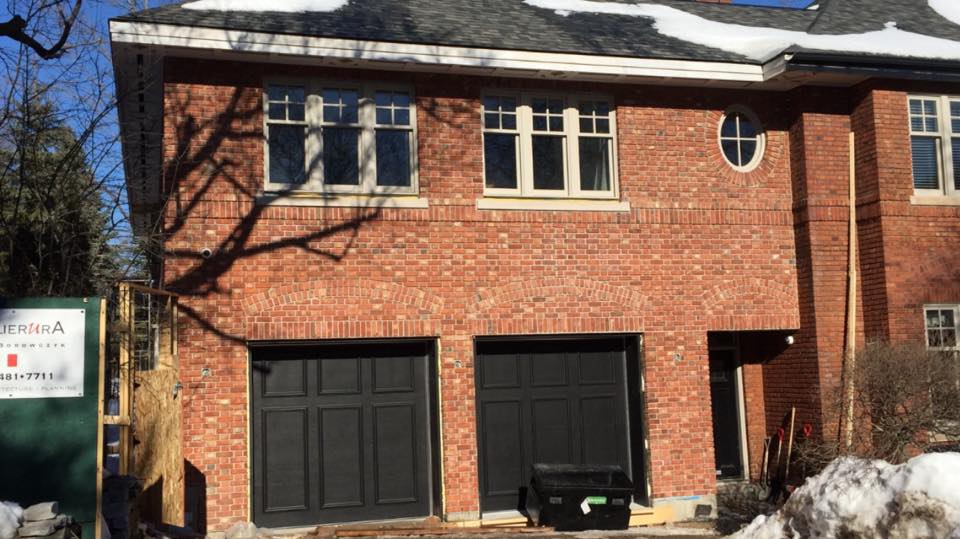Une maison en brique avec deux portes de garage et une enseigne devant.