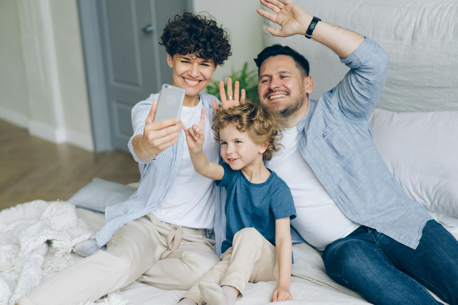 A family is sitting on a couch taking a selfie with a cell phone.