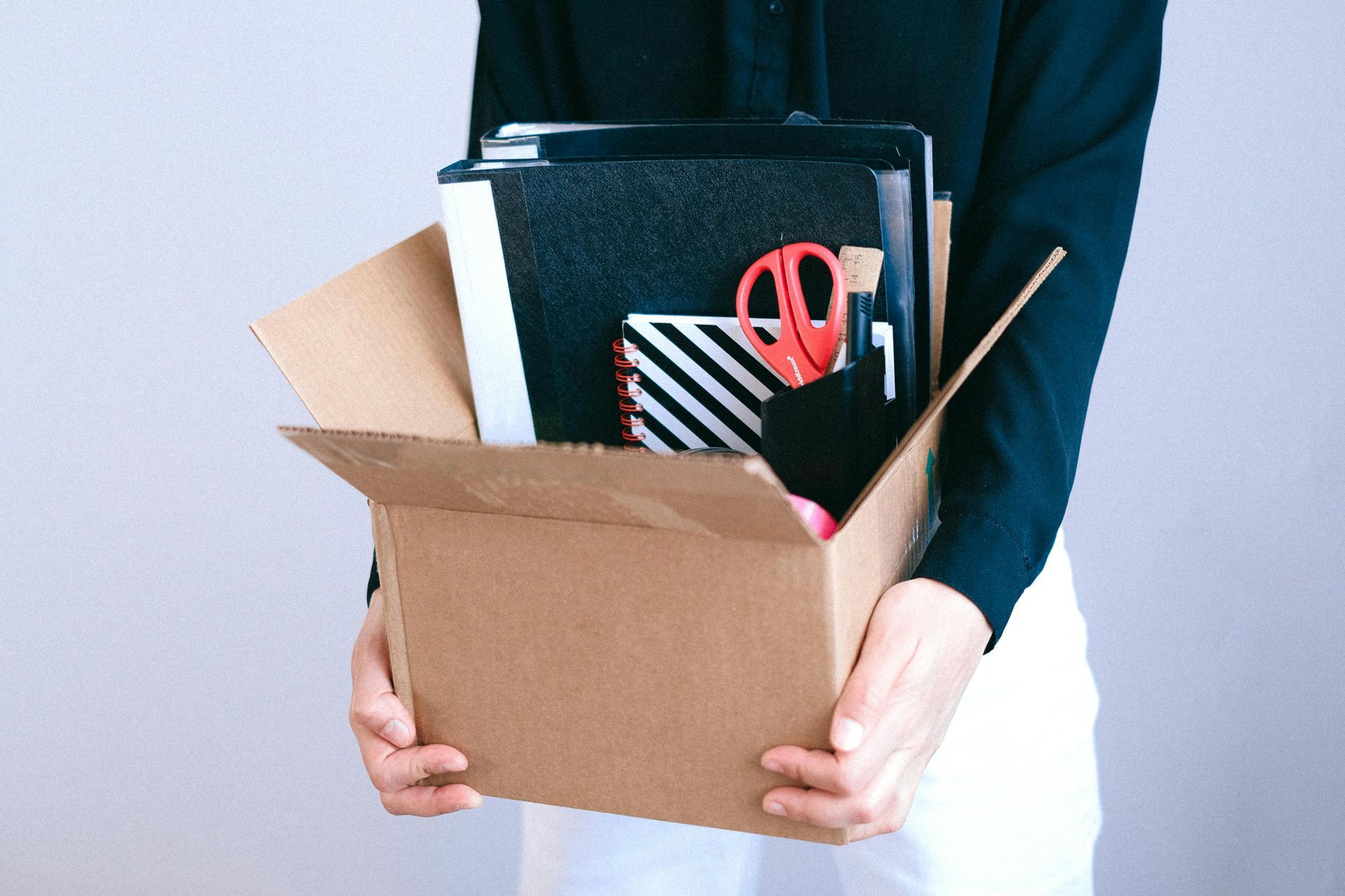 A woman is holding a cardboard box filled with office supplies.