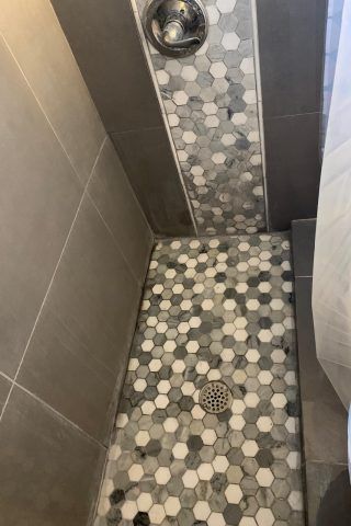 A shower with a hexagonal tile floor and a drain.