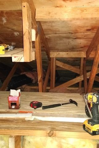 A wooden table with a hammer , tape measure , and a drill on it.