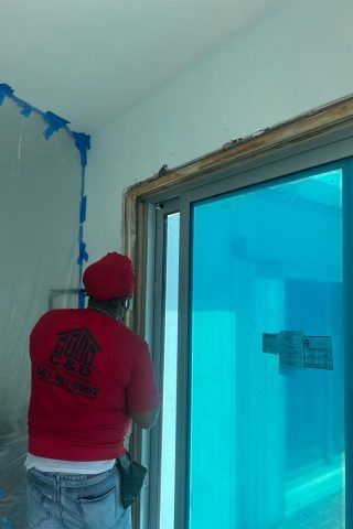 A man in a red shirt is working on a sliding glass door.