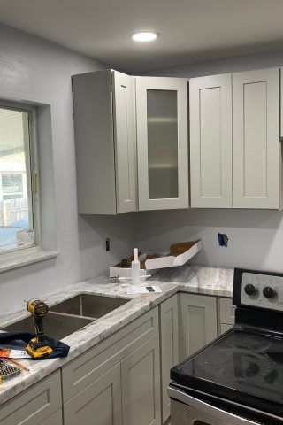 A kitchen with white cabinets , a sink , a stove and a window.