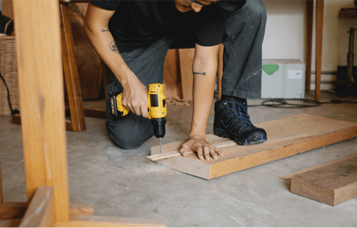 A man is using a drill to drill a hole in a piece of wood.