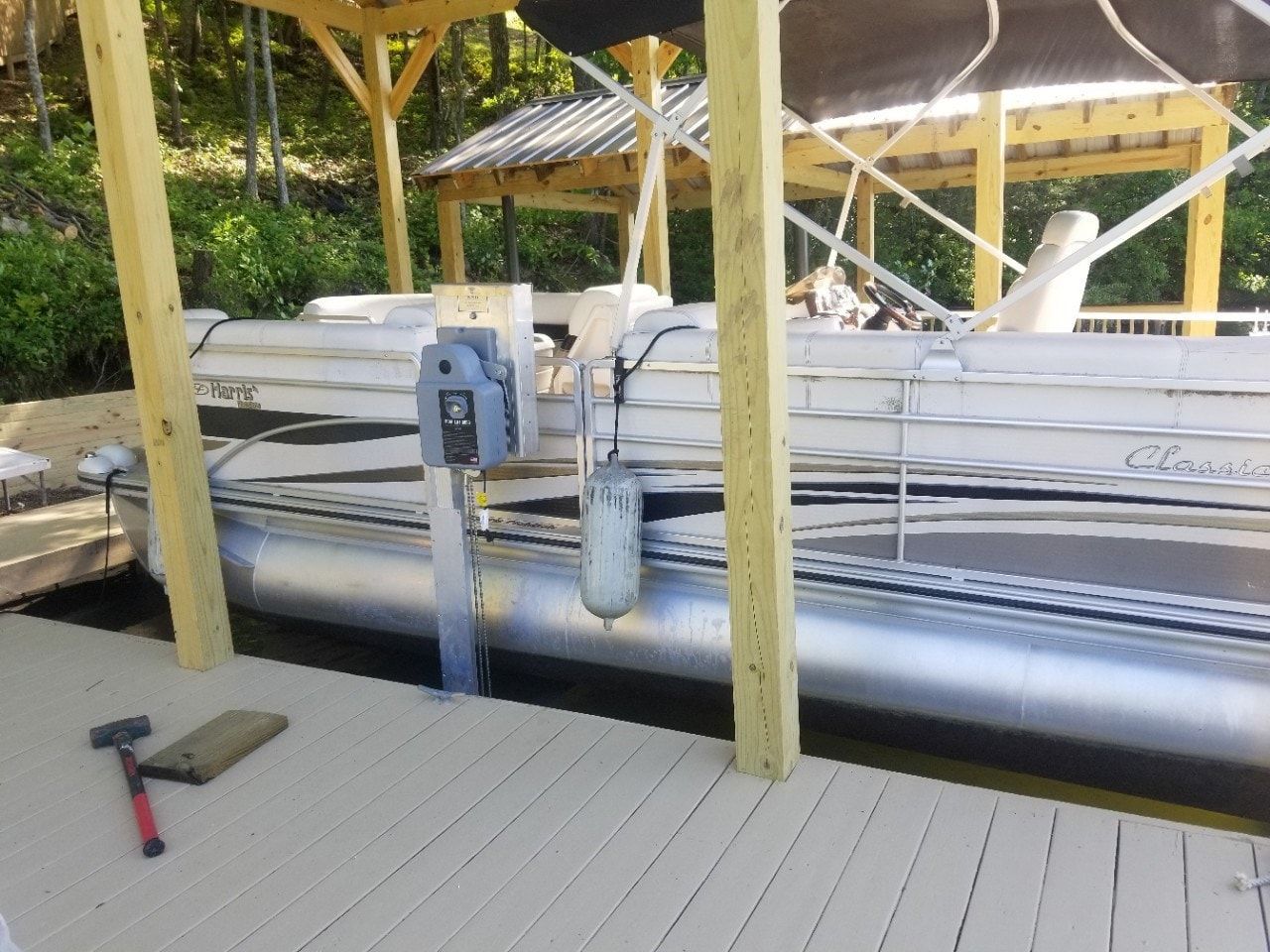 A pontoon boat is docked at a dock under a canopy.
