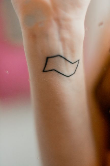 A forearm with a small black outline tattoo of a wavy shape near the wrist.