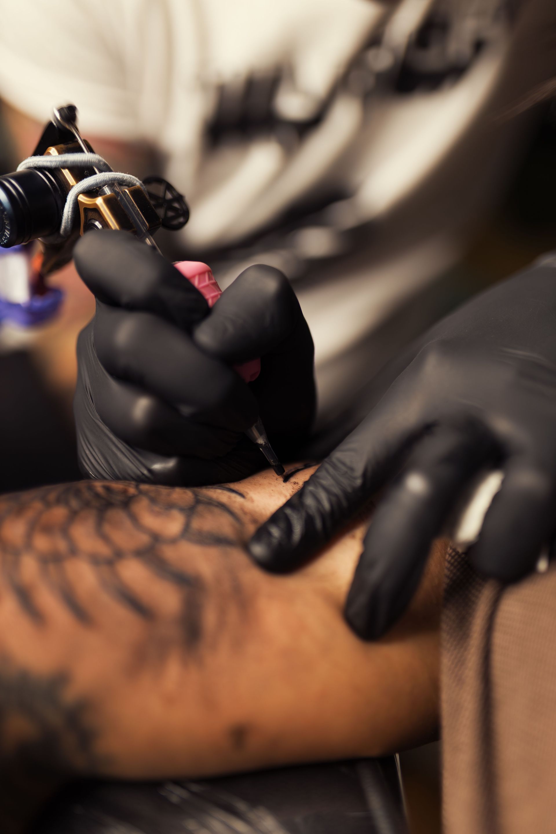Tattoo artist in black gloves using a tattoo machine on a client’s arm