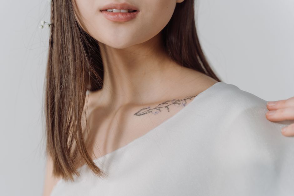 Close-up of a woman in a white top showing a delicate collarbone tattoo
