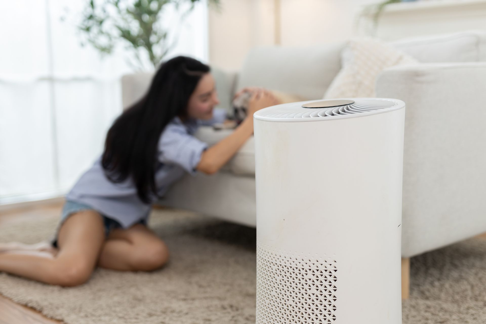 White air purifier in living room with person kneeling near a sofa.