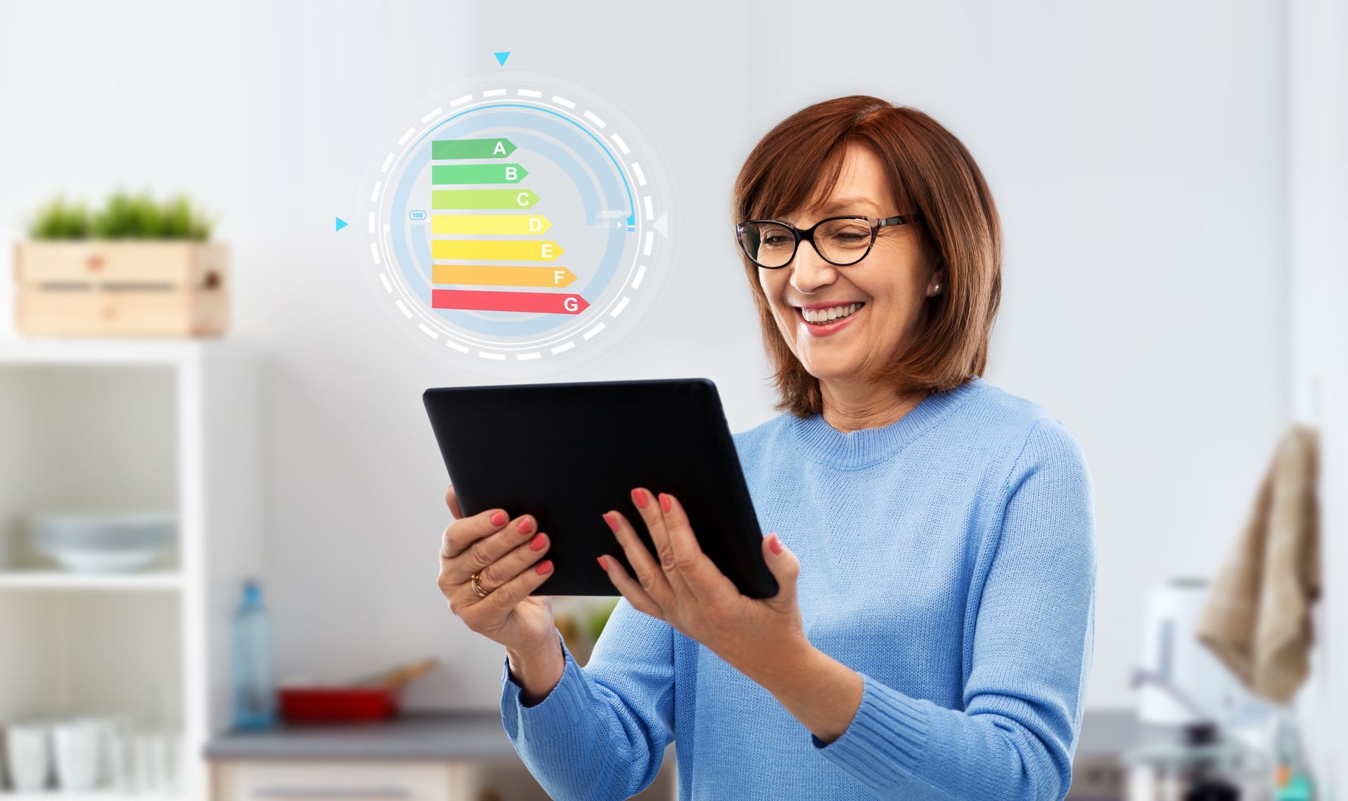 Woman holding tablet, smiling at energy efficiency chart in kitchen.