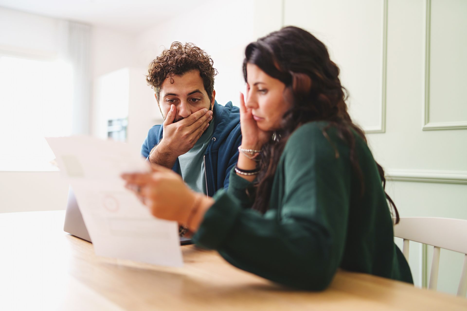 Couple looks distressed at a document. Man covers his mouth; woman holds her head.