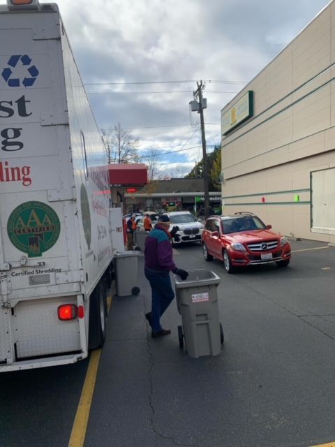 A man is pushing a trash can in front of a recycling truck
