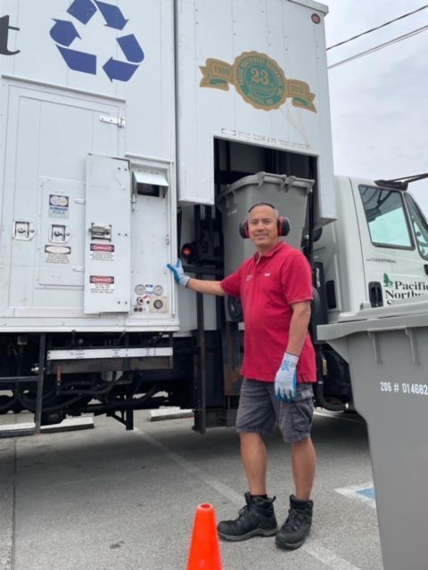 A man wearing headphones stands in front of a recycling truck