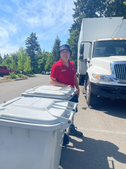 A man in a red shirt is pushing a trash can in front of a truck