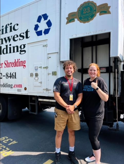 A man and a woman are standing in front of a pacific northwest shredding truck