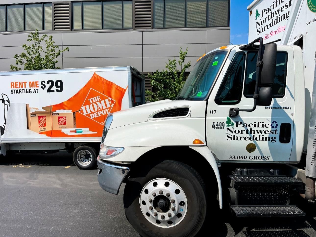A home depot truck is parked next to a pacific northwest shredding truck