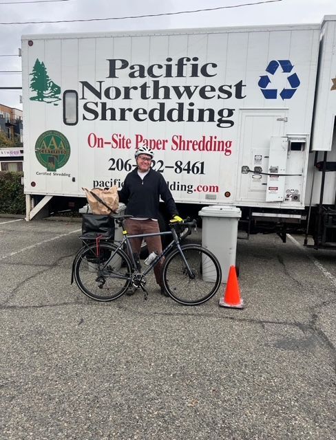 A man standing next to a bicycle in front of a pacific northwest shredding truck
