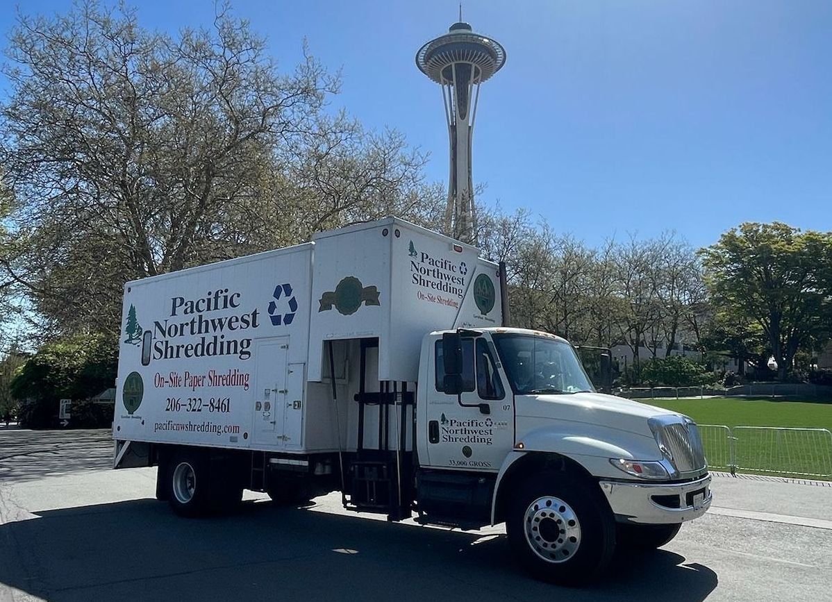 A white pacific northwest recycling truck is parked on the side of the road.
