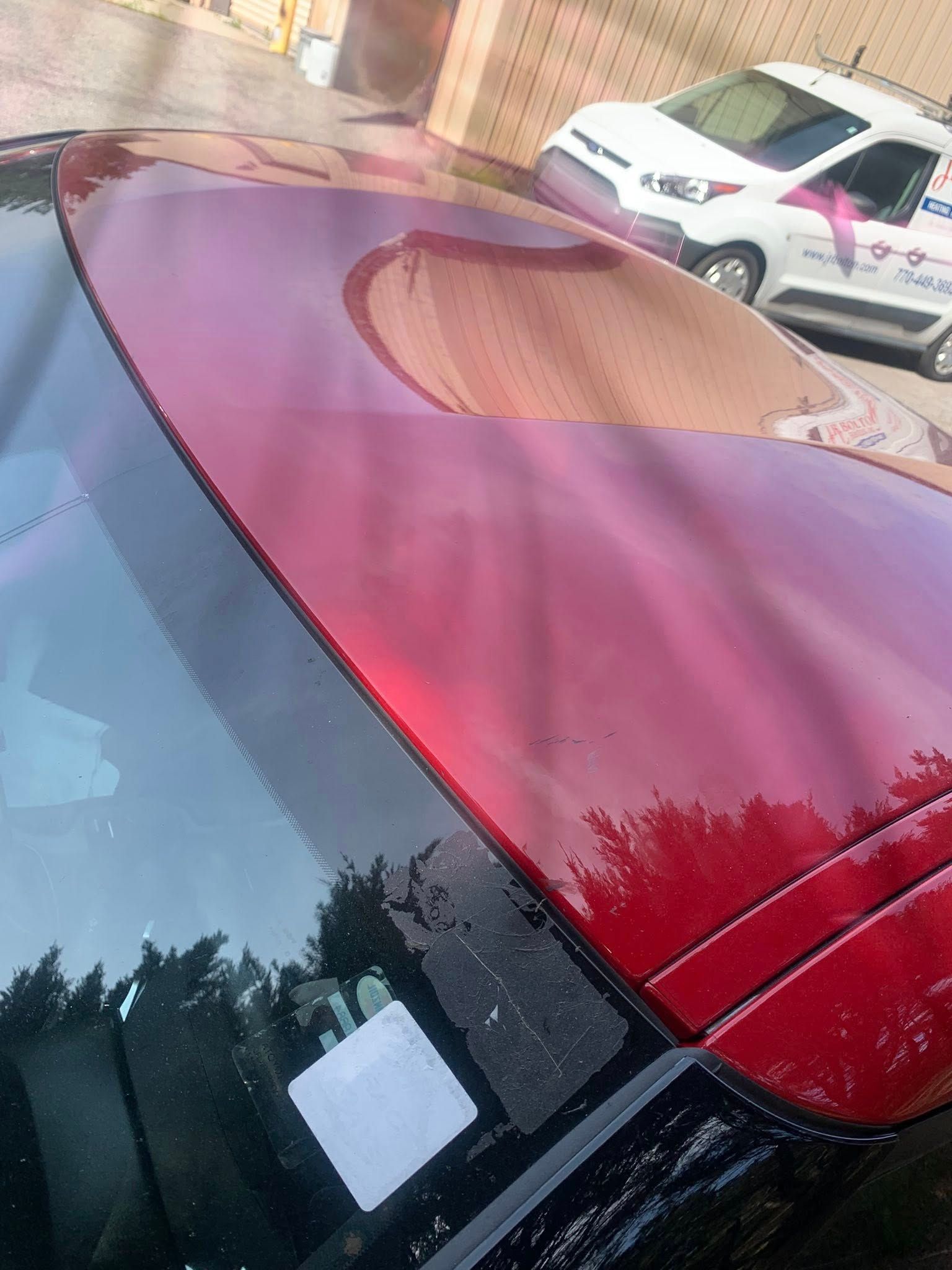 Red car roof, windshield, and white car in the background.