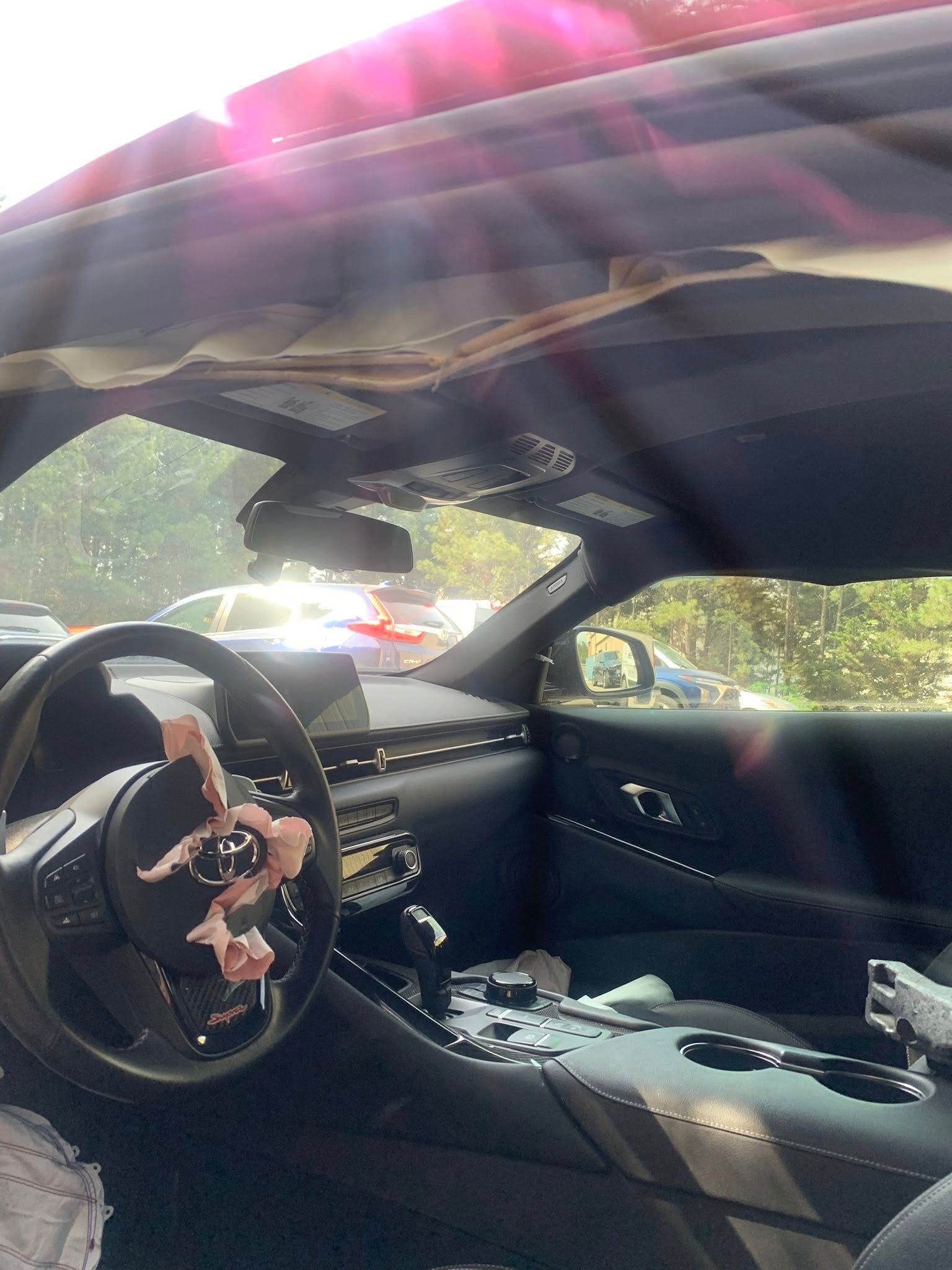 Interior of a damaged red sports car, airbag deployed. Sun shining through the roof.