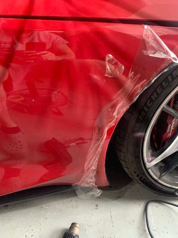 Red car with protective film being applied to its side panel. A person is reflected in the car.