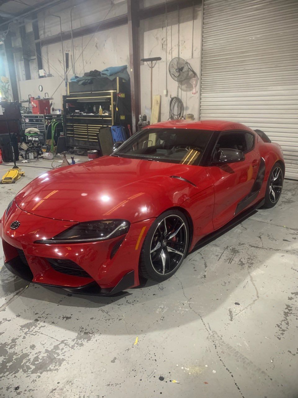 Red Toyota Supra sports car in a garage with tools and a closed bay door.