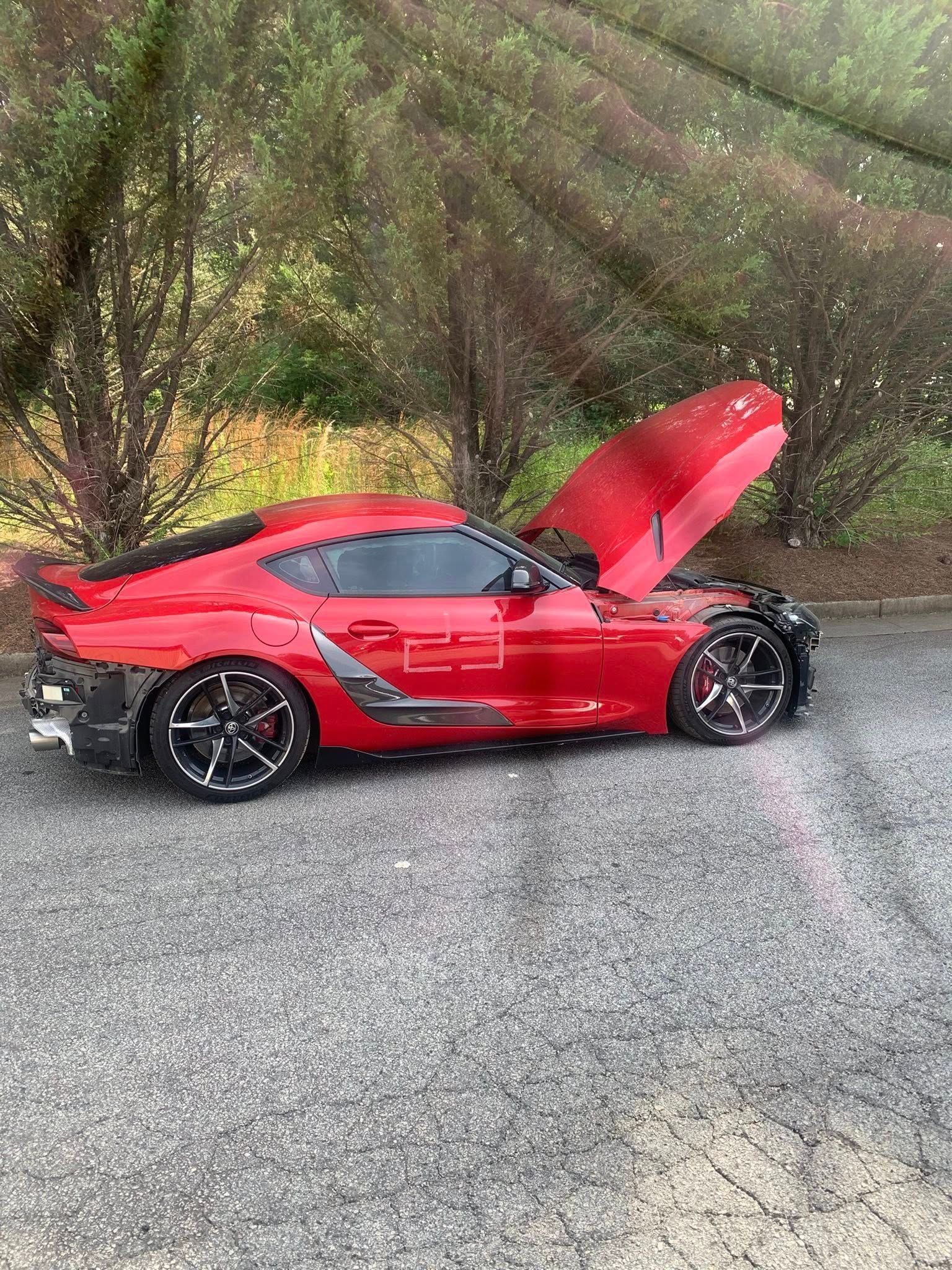 Red sports car with the hood open, parked outdoors on asphalt.