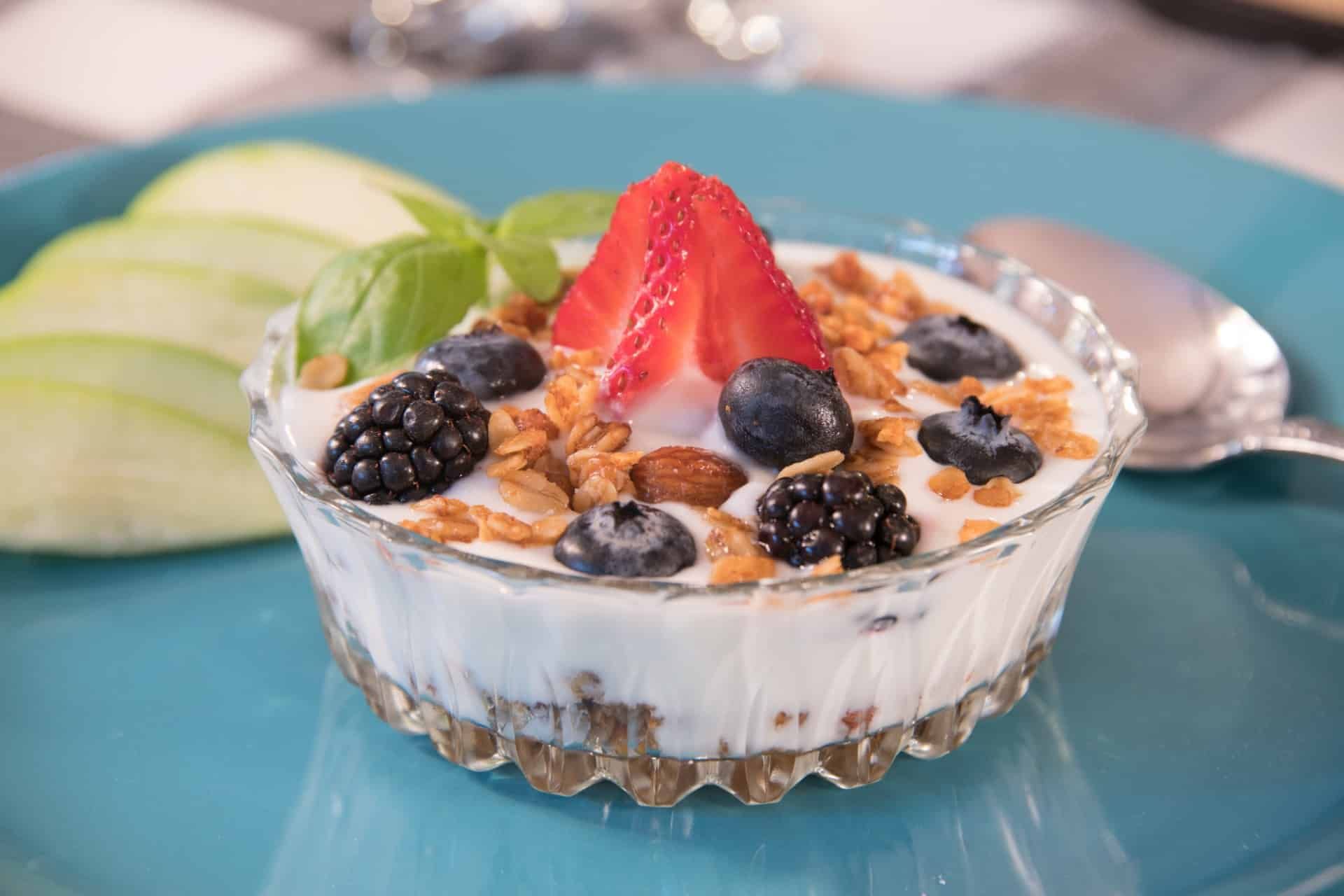 A bowl of yogurt with berries and granola on a blue plate with a spoon.