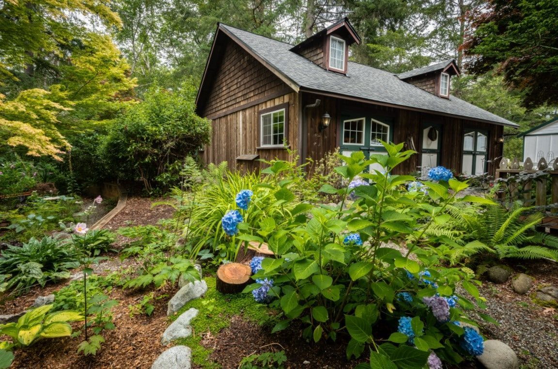 A small wooden house is surrounded by trees and flowers in a garden.