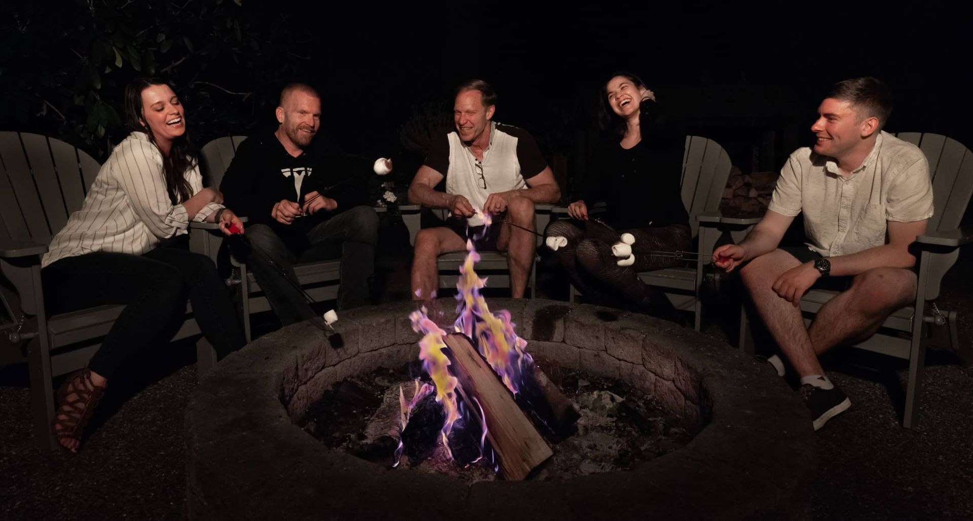 A group of people are sitting around a fire pit at night.