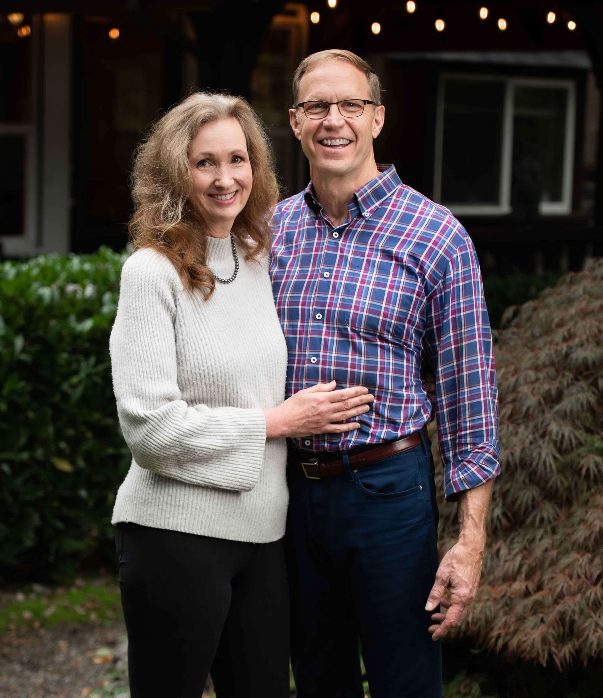 A man and a woman are posing for a picture in front of a house.