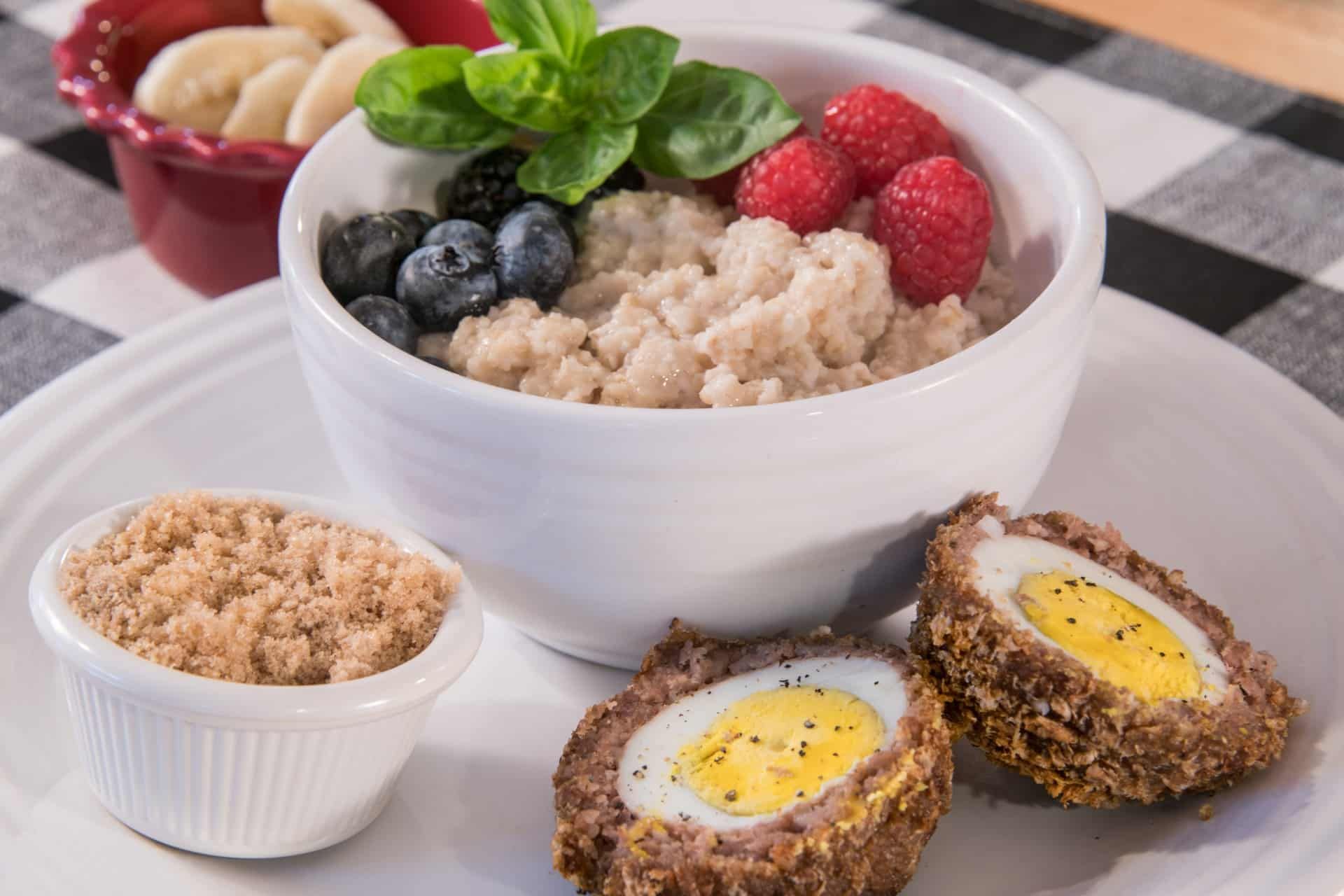 A bowl of oatmeal with raspberries , blueberries and a scotch egg on a plate.