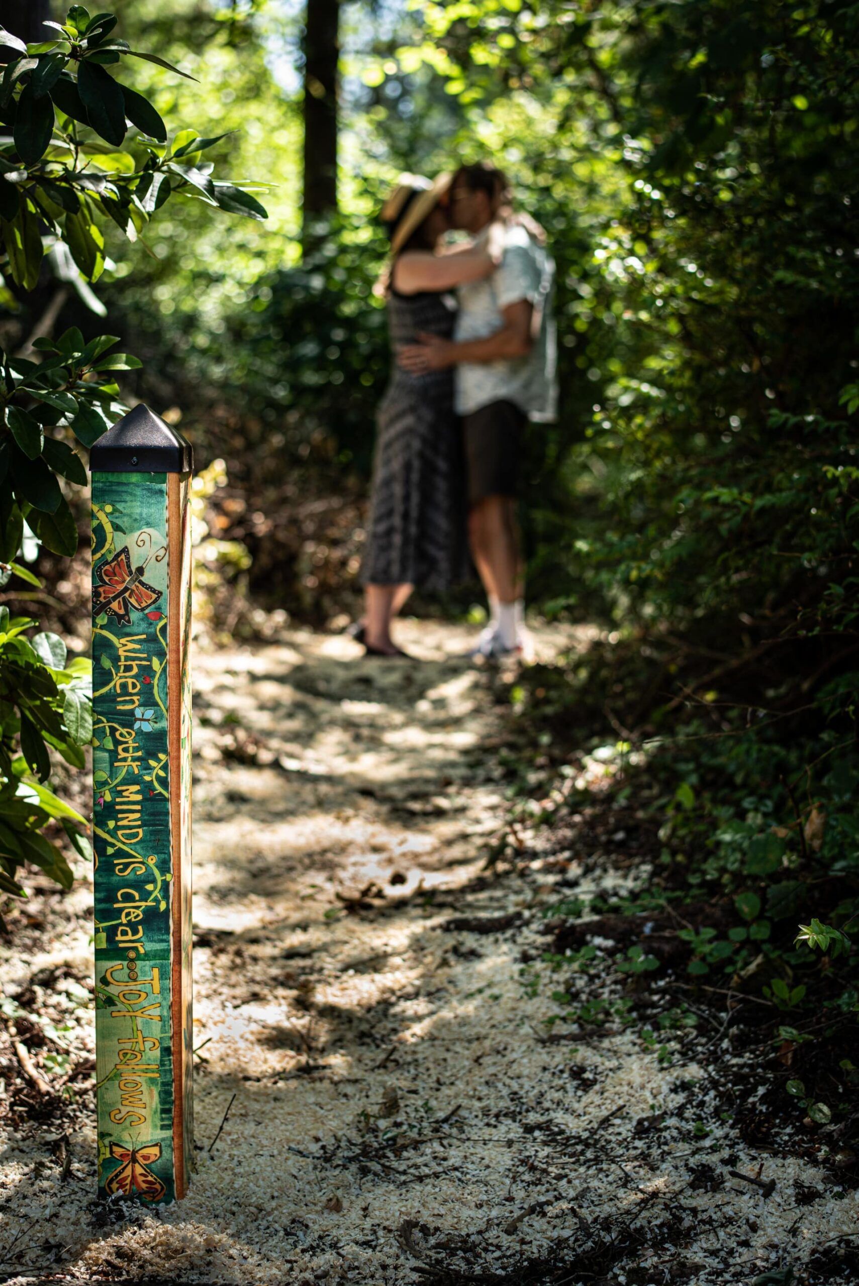 A man and woman are kissing on a path in the woods.