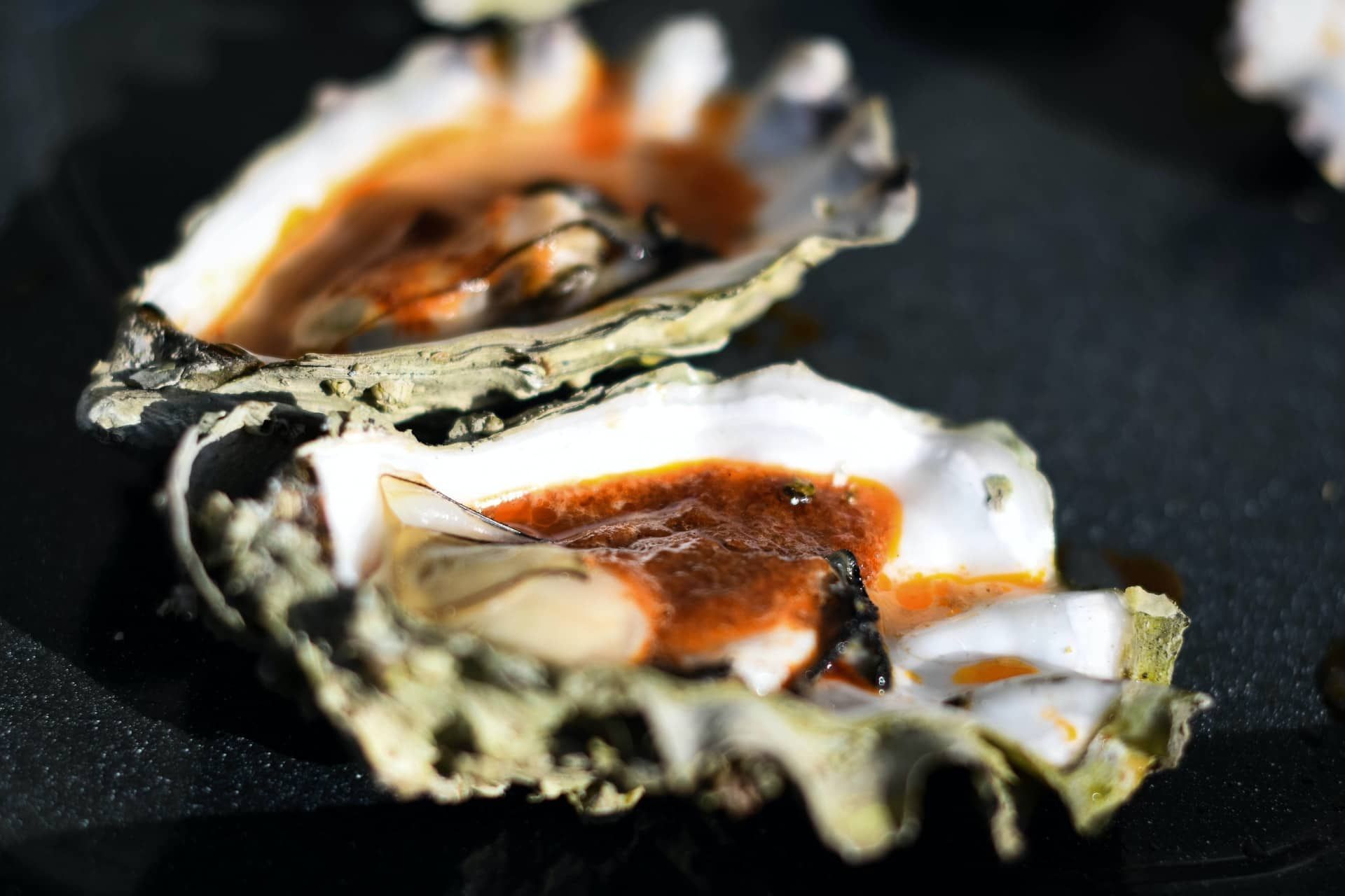 A close up of an oyster with sauce on it on a black plate.