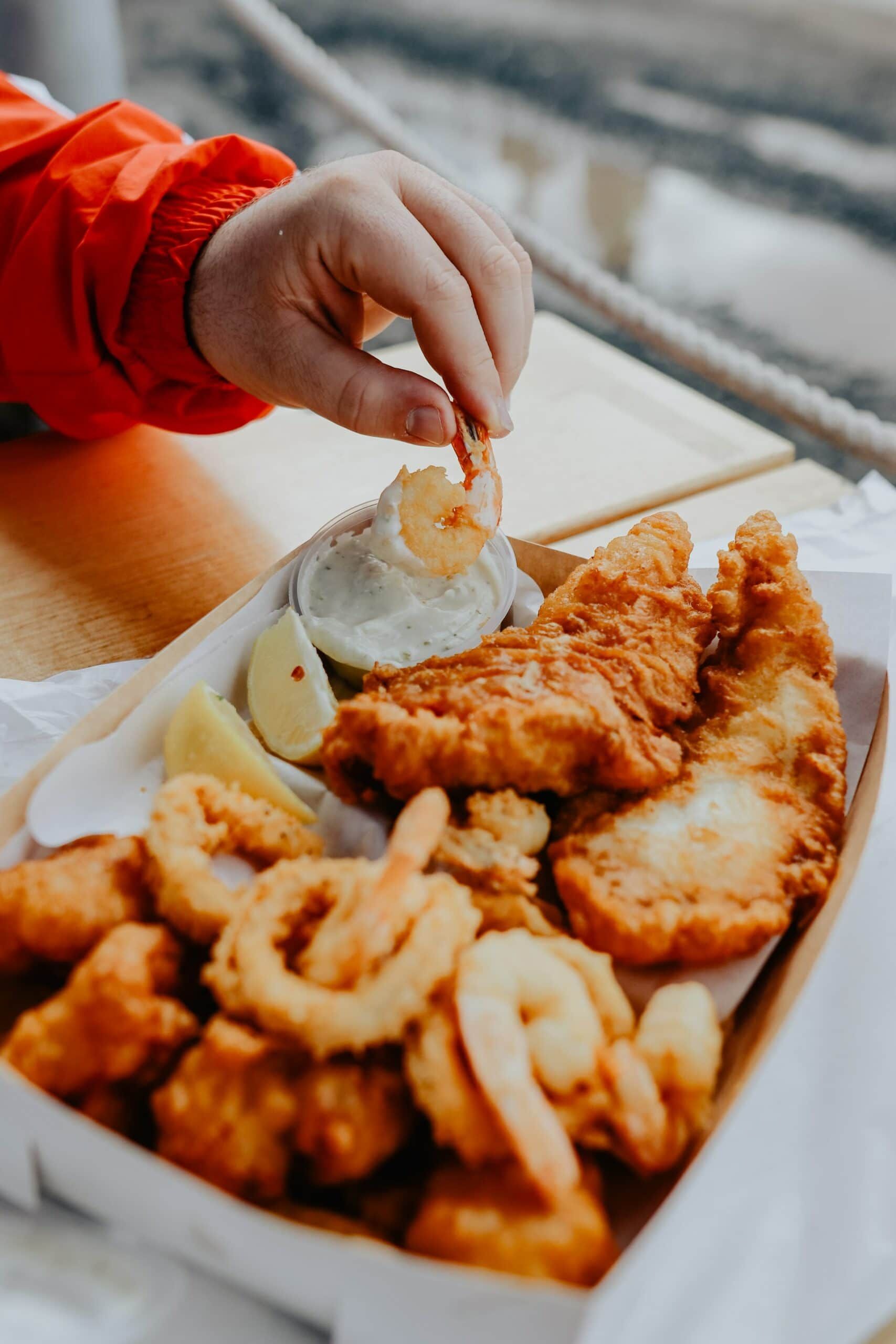 A person is dipping a shrimp into a container of fried food.