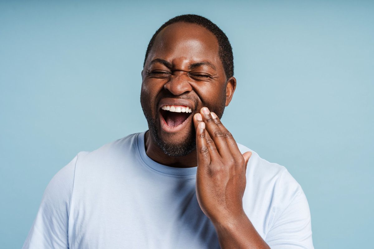 A man is laughing while holding his mouth in pain.