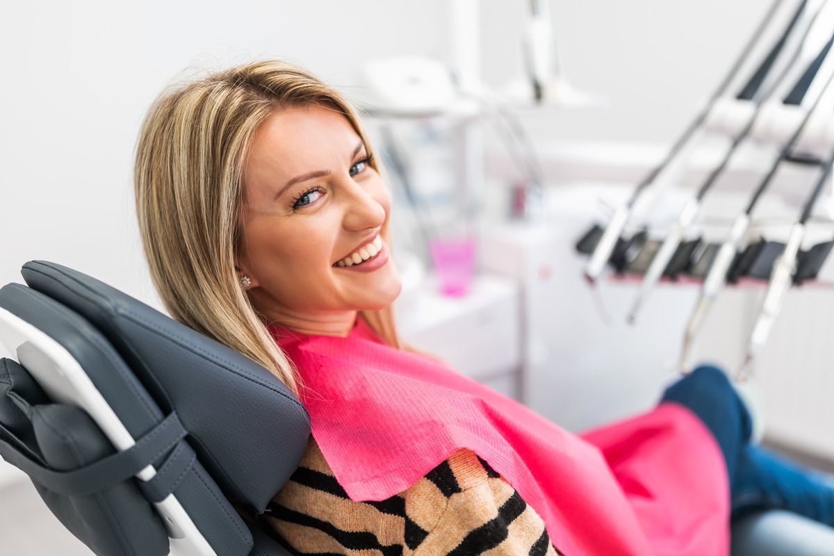 A woman is sitting in a dental chair and smiling.