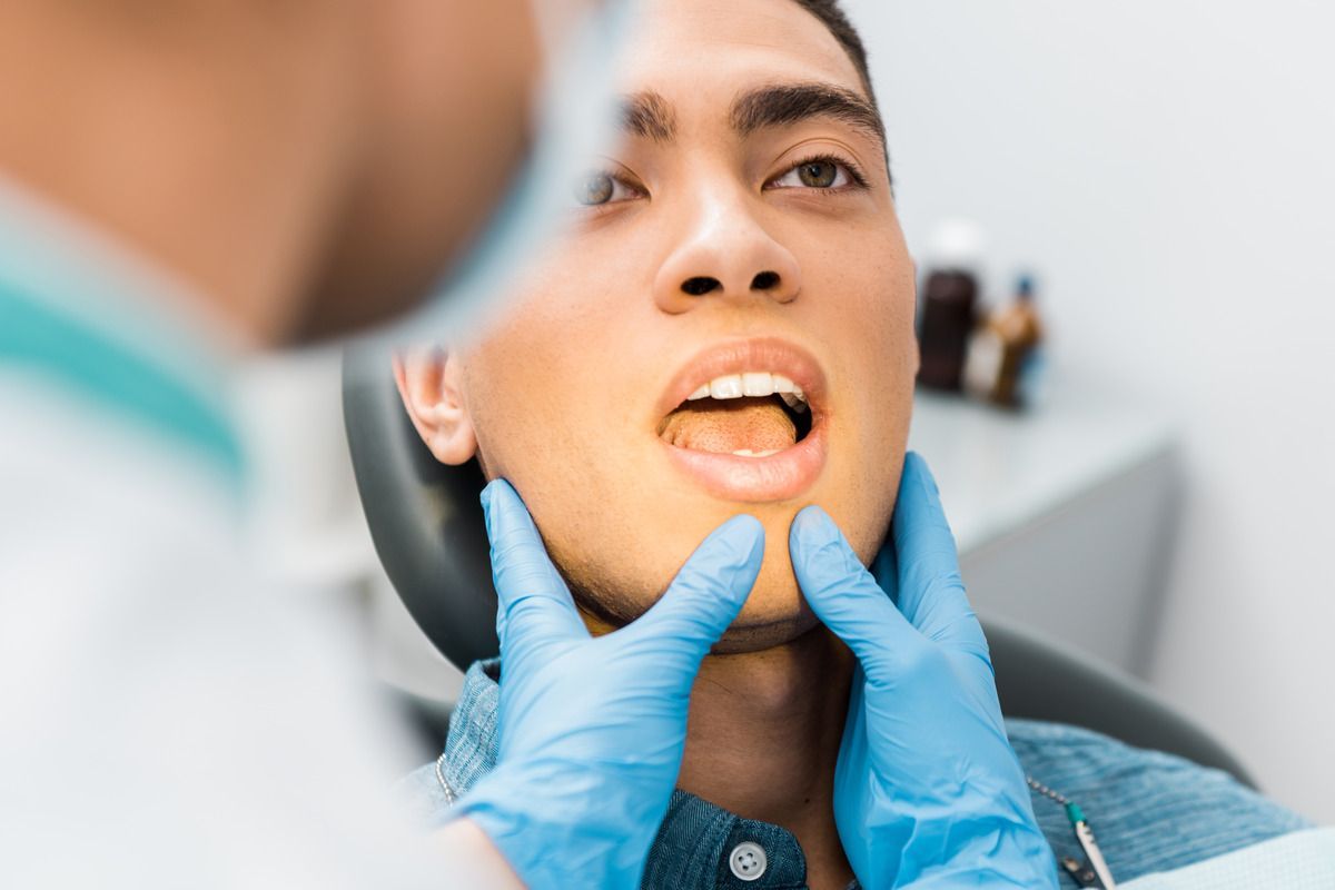 A man is sitting in a dental chair while a dentist examines his teeth.